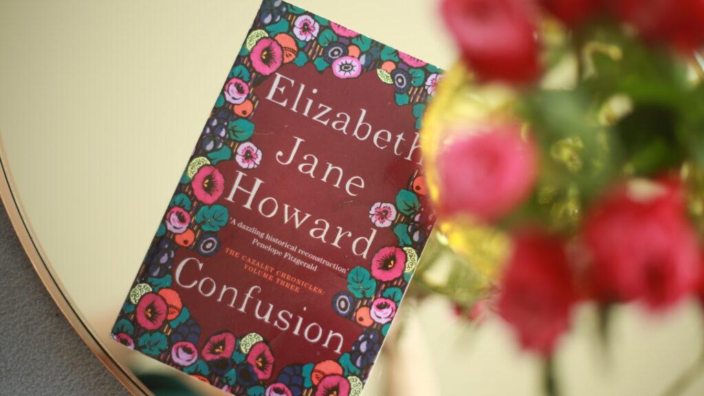 Photo of the novel Confusion by Elizabeth Jane Howard, with delicate, blurred flowers in the foreground adding a soft, romantic atmosphere.