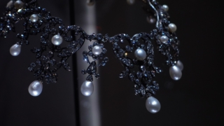 Close-up of an elegant pearl necklace with round, lustrous white pearls strung softly reflecting light against a black background.