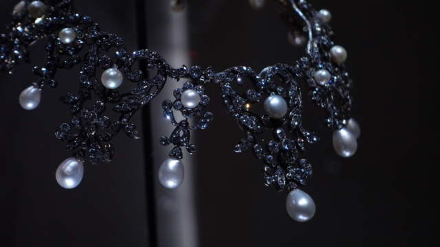 Close-up of an elegant pearl necklace with round, lustrous white pearls strung softly reflecting light against a black background.