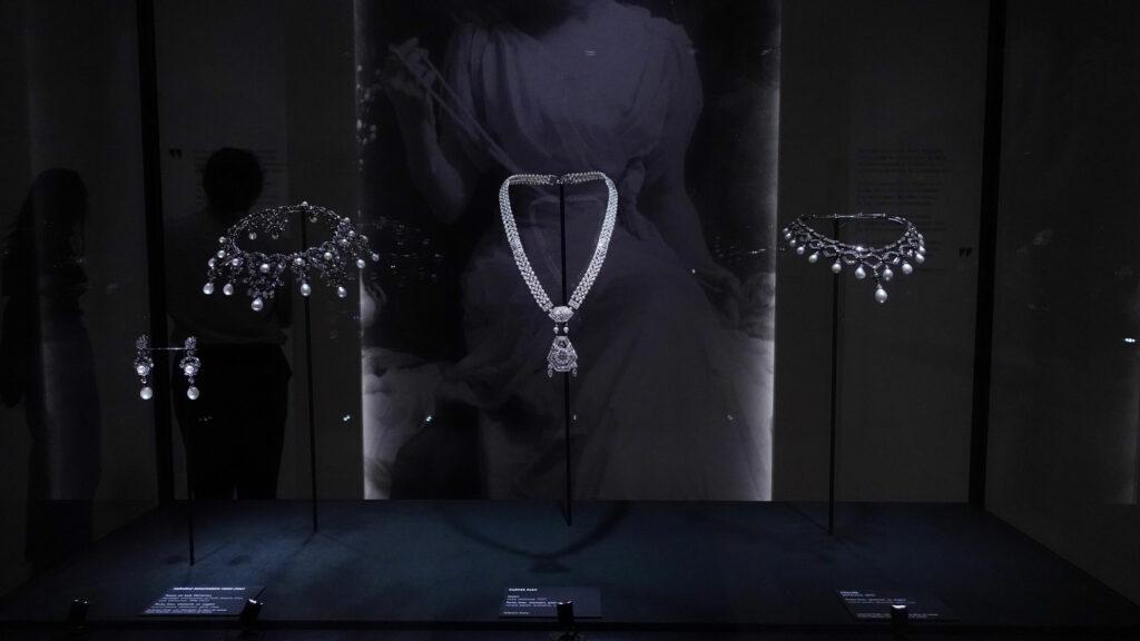 Photo from a jewelry exhibition showing a glass display case containing several elegant necklaces and pairs of earrings, all carefully arranged under soft lighting.