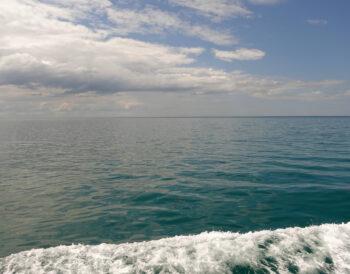 sea scape with white clouds in the sky, a dark green-blue sea and a wave of foam from the boat in the foreground