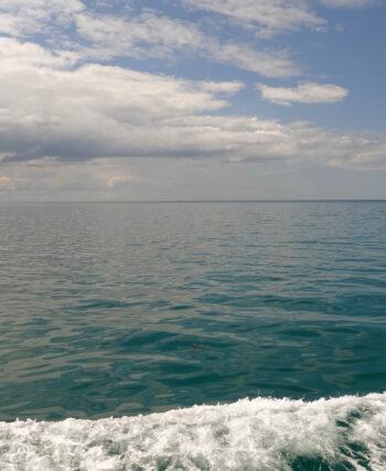 sea scape with white clouds in the sky, a dark green-blue sea and a wave of foam from the boat in the foreground