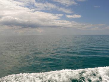 sea scape with white clouds in the sky, a dark green-blue sea and a wave of foam from the boat in the foreground