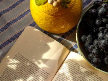 An open book, black grapes in a bowl and a ceramic lemon bowl
