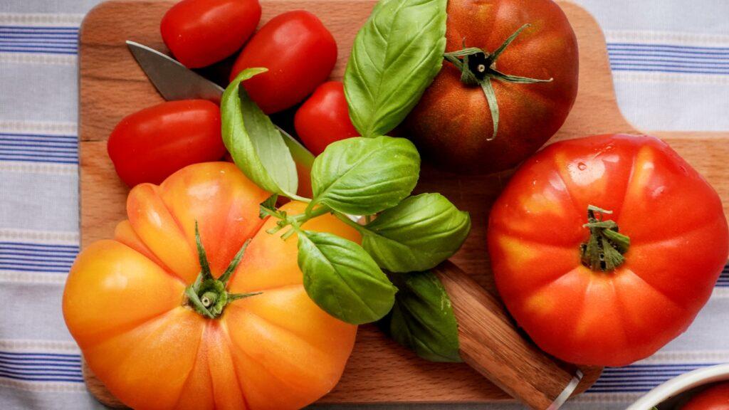 Italian tomatoes of several colours on a chopping board with fresh leaves of basil