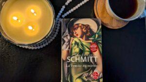 A copy of Eric-Emmanuel Schmitt's novel Three Women in a Mirror (La Femme au miroir) as a quiet reading ritual with coffee and candles.