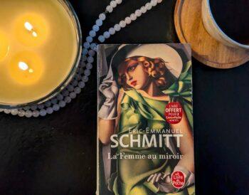 A copy of Eric-Emmanuel Schmitt's novel Three Women in a Mirror (La Femme au miroir) as a quiet reading ritual with coffee and candles.