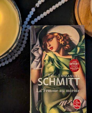 A copy of Eric-Emmanuel Schmitt's novel Three Women in a Mirror (La Femme au miroir) as a quiet reading ritual with coffee and candles.