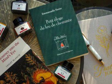 A stack of winter books including Journey into the Mind’s Eye by Lesley Blanch and Petit éloge du feu de cheminée by Emmanuelle Favier on a wooden table