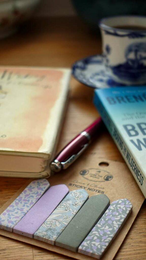 An atmospheric photo of a book open next to a steaming cup of coffee, a classic fountain pen, and a notepad with yellow sticky notes, capturing a quiet morning of reading and reflection.