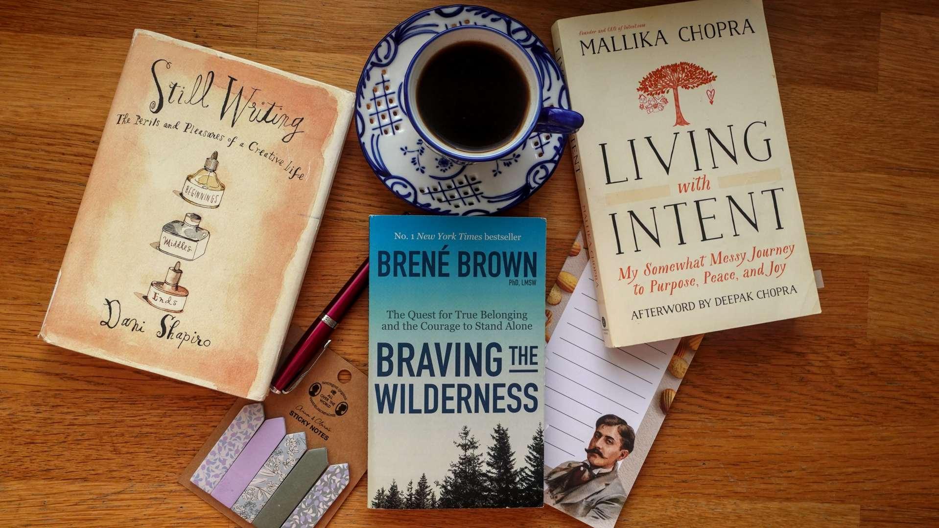 A top-down flat lay of three books: Living with Intent by Mallika Chopra, Braving the Wilderness by Brené Brown, and Still Writing by Dani Shapiro, arranged neatly on a wooden surface.