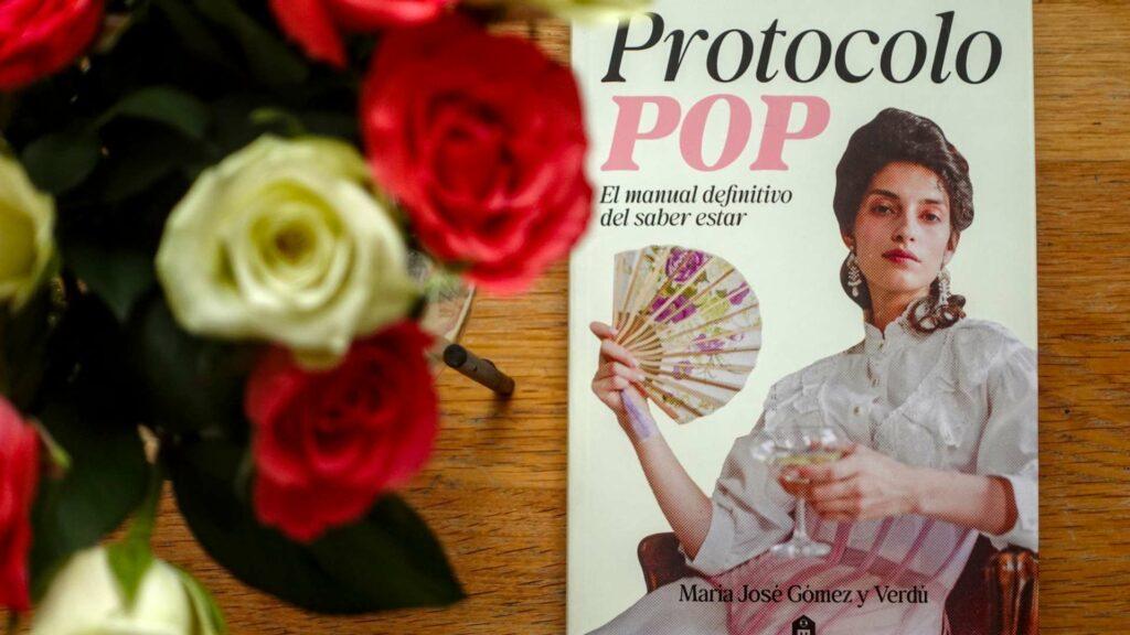 A vibrant flatlay of the book Protocolo Pop by María José Gómez y Verdú surrounded by blooming flowers.