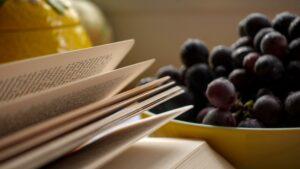 An open book resting beside a bowl of fresh grapes, evoking the pleasures of slow reading and quiet afternoons