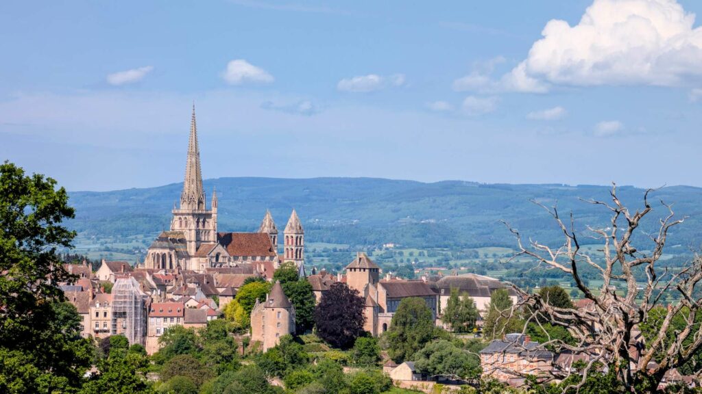 Panoramic view of Autun with the Saint-Lazare Cathedral rising above the medieval rooftops against a blue sky and rolling hills