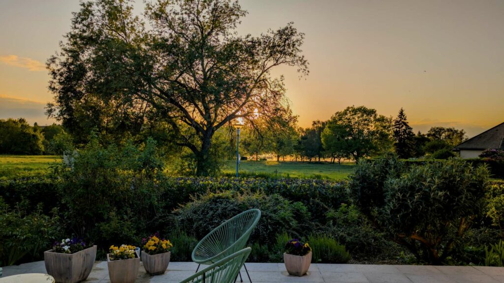 Golden sunset over the Burgundy countryside seen from a garden terrace with a green chair and flowering pots in the foreground