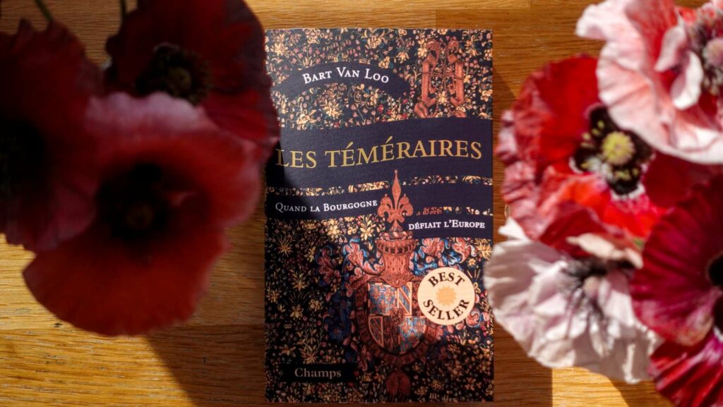 Copy of The Burgundians by Bart Van Loo surrounded by red poppies on a wooden table