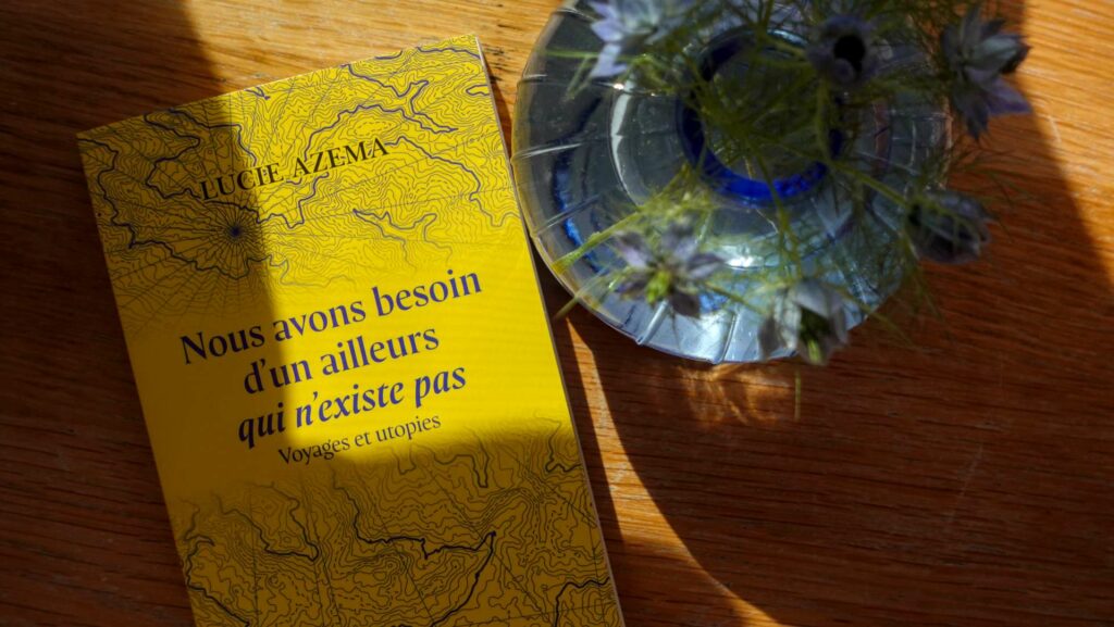 Bright yellow cover of Nous avons besoin d'un ailleurs qui n'existe pas by Lucie Azema beside a crystal vase of blue wildflowers