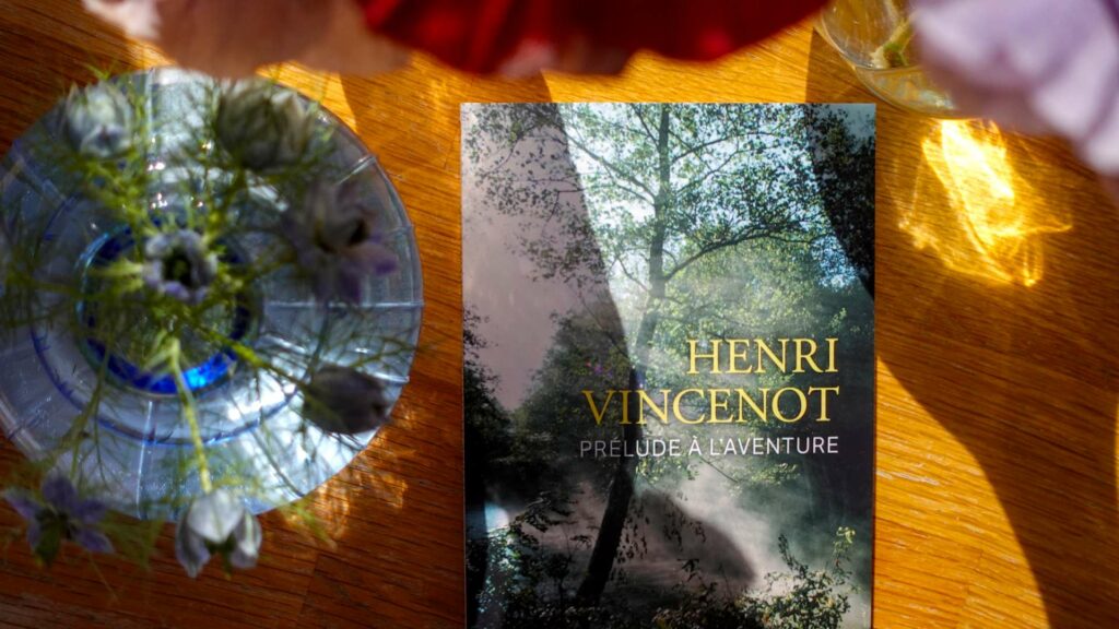 Prélude à l'aventure by Henri Vincenot beside a glass vase of wildflowers in afternoon light